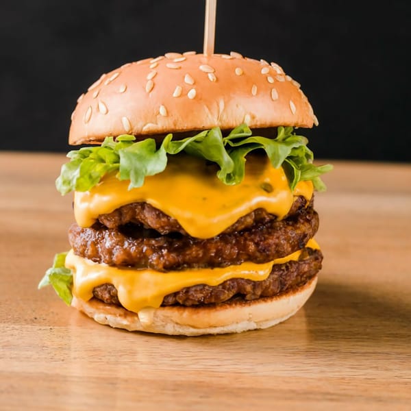 A towering double cheeseburger with melted cheese, lettuce, and a sesame seed bun on a wooden surface.