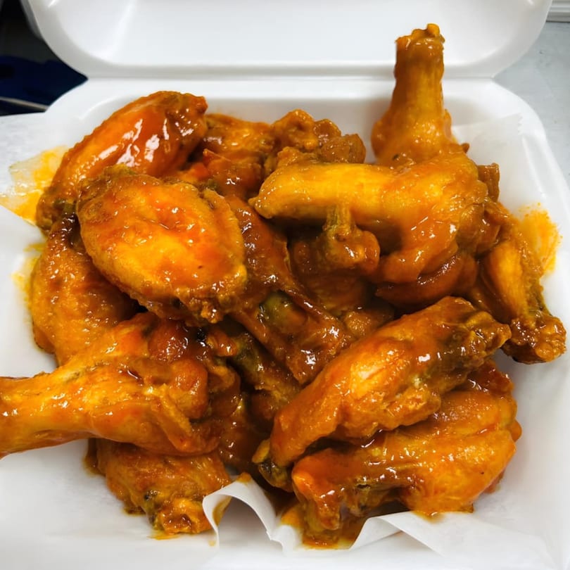 A white takeout container filled with a generous serving of saucy, orange chicken wings.