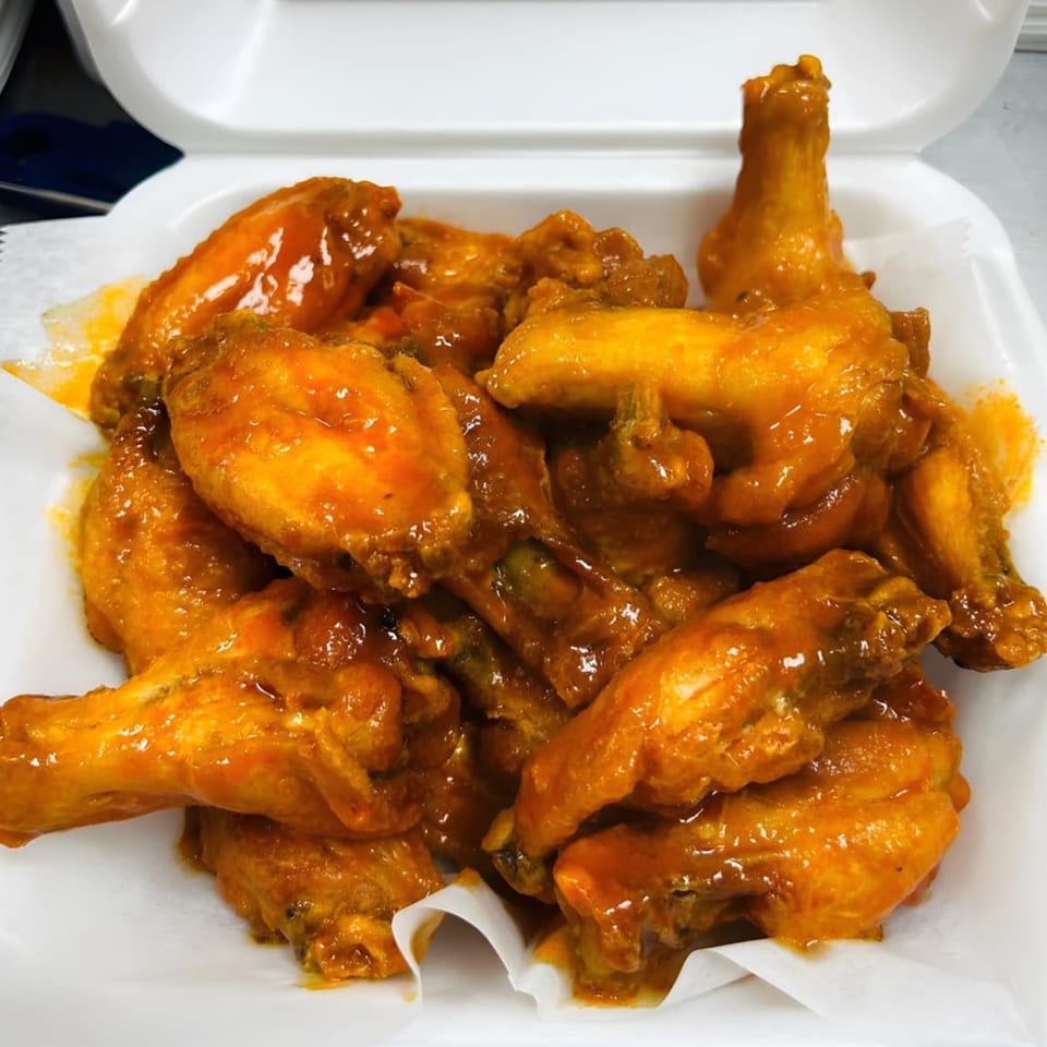 A white takeout container filled with a generous portion of glistening, orange-sauced chicken wings.