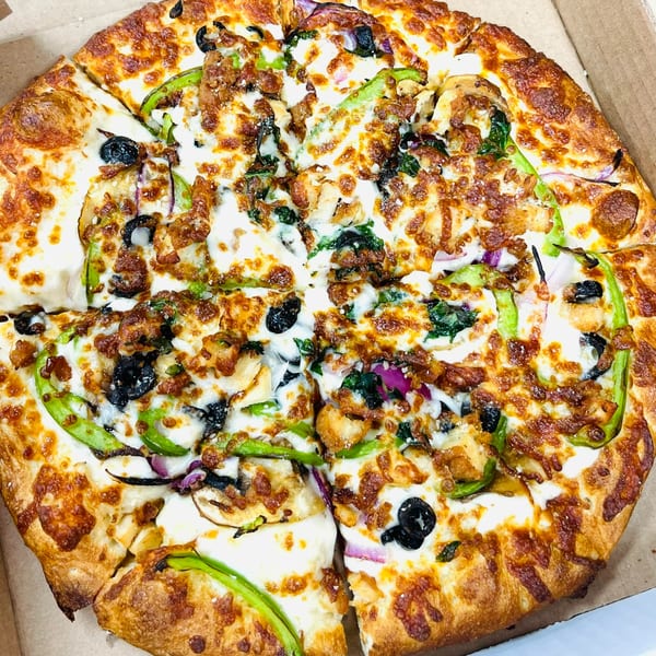 A whole AJ'S GRAB N GO pizza with green peppers, black olives, and chicken in a box.