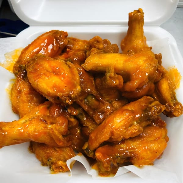 A white takeout container filled with a generous serving of AJ's Grab N Go buffalo wings.