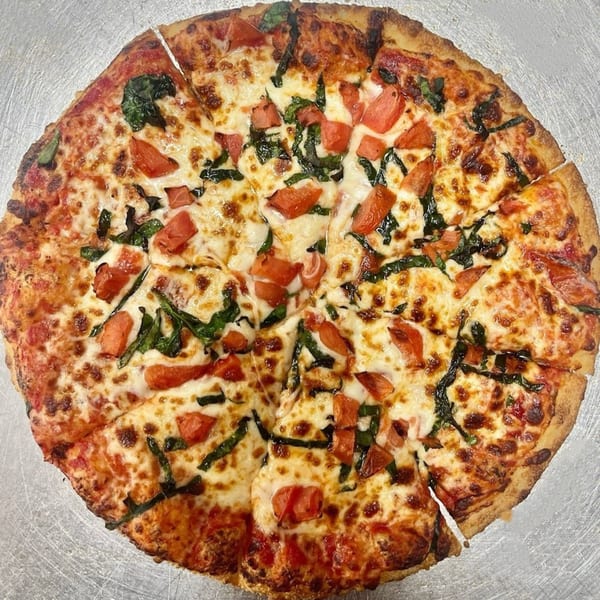 A freshly baked AJ'S GRAB N GO pizza, sliced, topped with melted cheese, diced tomatoes, and basil.