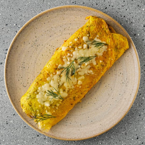 Golden omelet topped with melted cheese and fresh dill sprigs on a speckled plate.